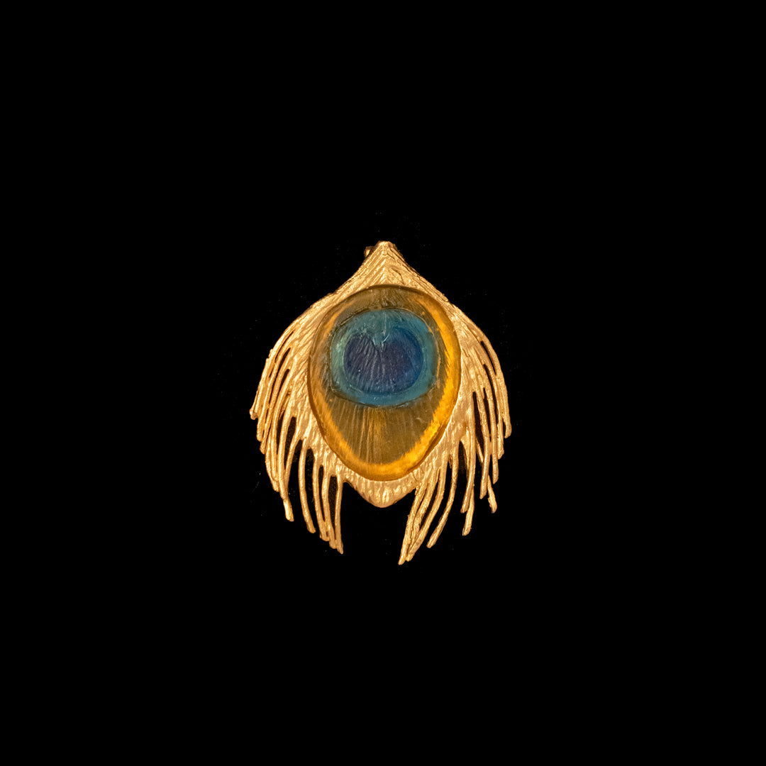 A bronze brooch with a gold finish and blue glass accent, displayed against a black background.