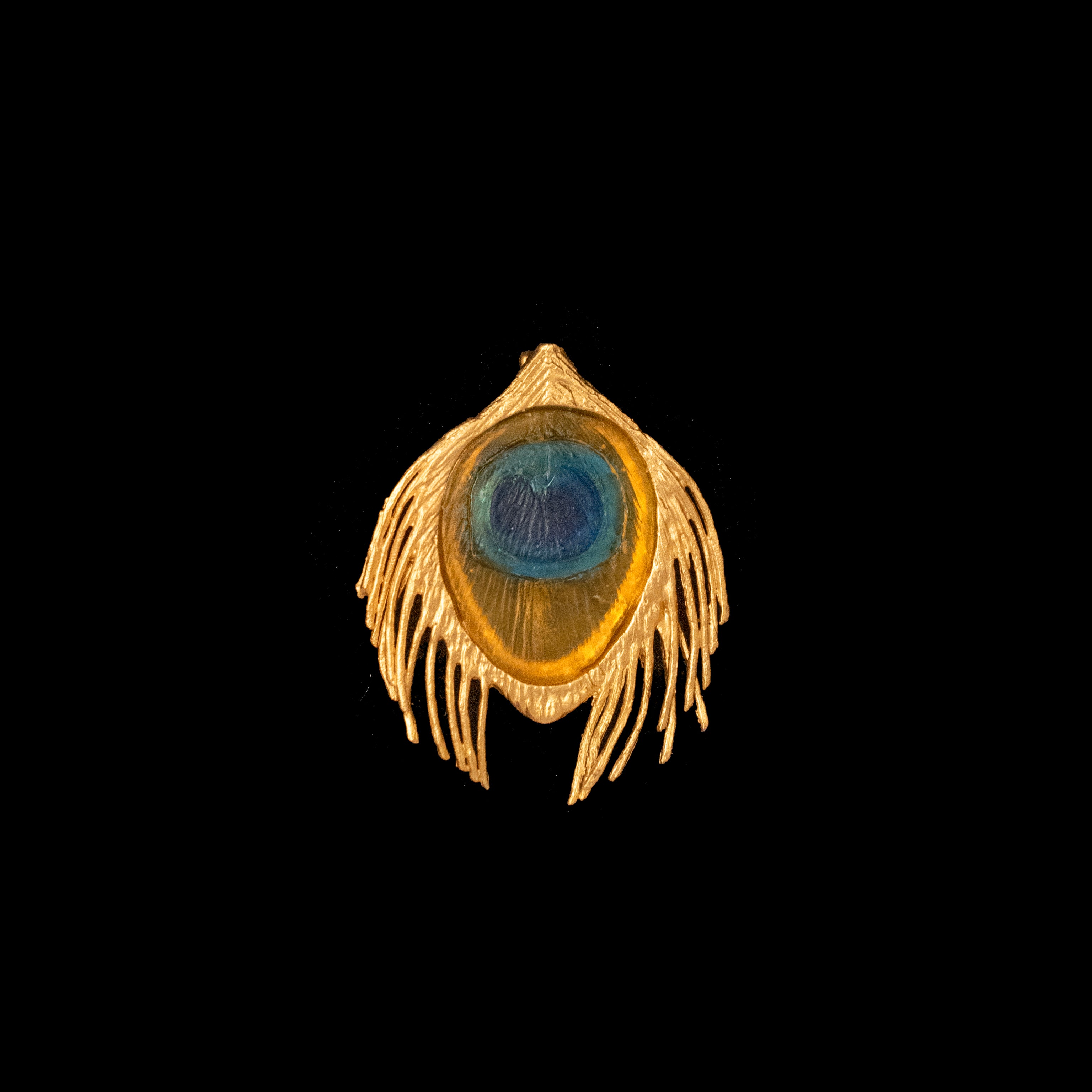 A bronze brooch with a gold finish and blue glass accent, displayed against a black background.