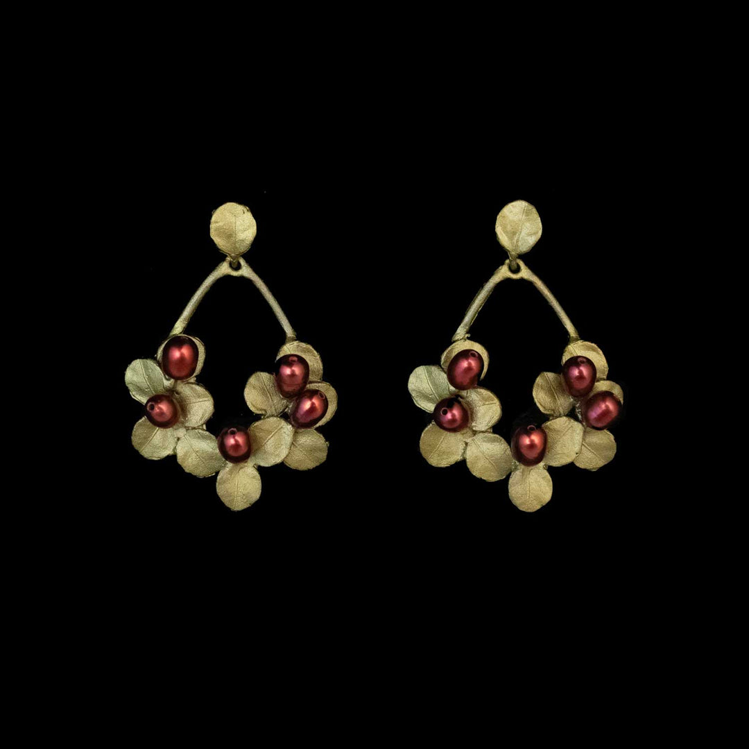 A pair of Firethorn earrings in a teardrop shape with green leaves and red freshwater pearls at the bottom of the loop, set against a black background.