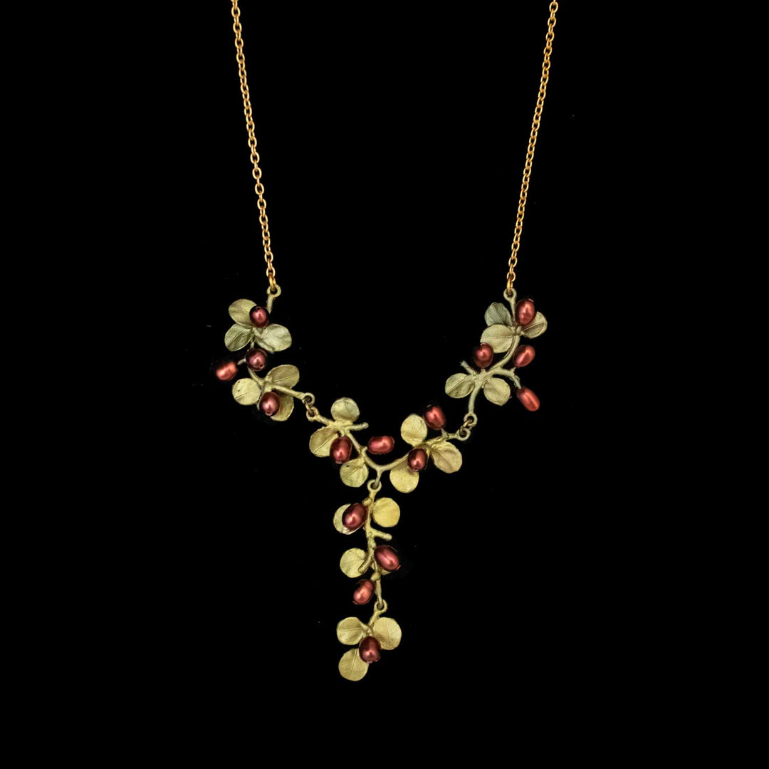 The Firethorn Necklace is a green Y-shaped pendant with bronze leaves and red freshwater pearl clusters, arranged like a vine, displayed against a black background.