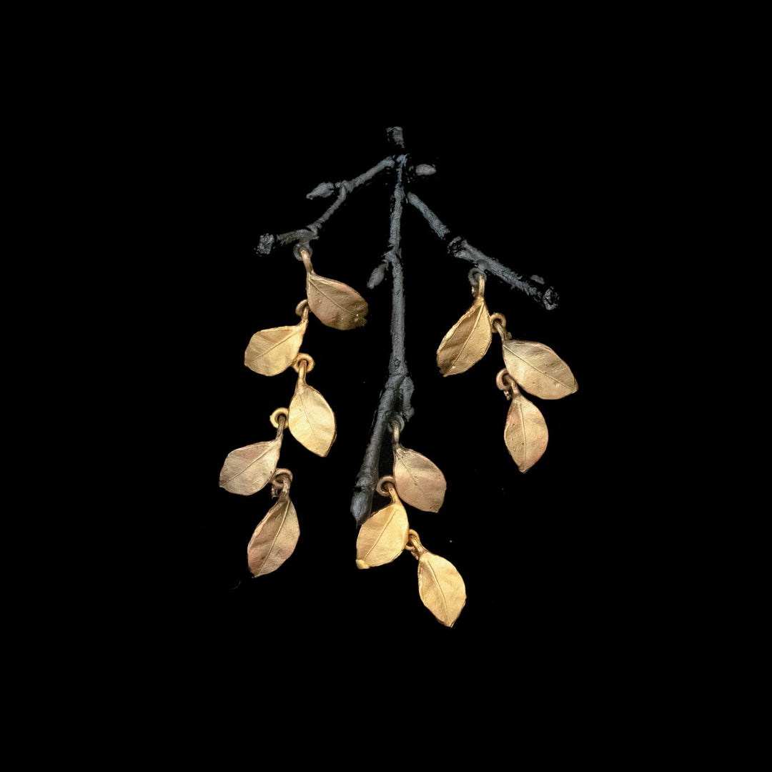 A brooch featuring gold-toned metal leaves suspended from a dark, branch-like structure against a black background.
