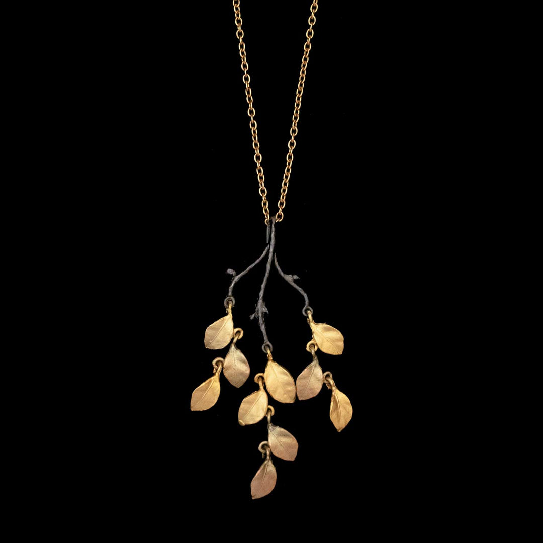 The Golden Autumn Pendant is a 24kt gold-plated necklace with a branch-shaped pendant featuring multiple gold leaves, inspired by birch leaf jewelry, set against a striking black background.