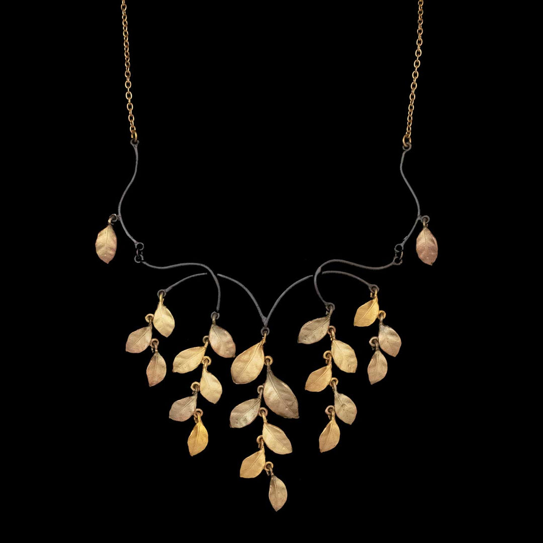 The Golden Autumn Necklace - Statement features gold and bronze-toned metal leaves, cascading from brown curved branches on a gold chain, elegantly displayed against a black background.