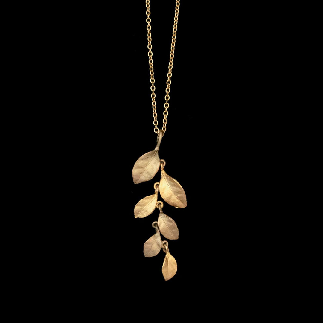 A gold and antique bronze plated pendant necklace with a vertical branch design, featuring five birch leaf jewelry accents of varying sizes, displayed against a solid black background.