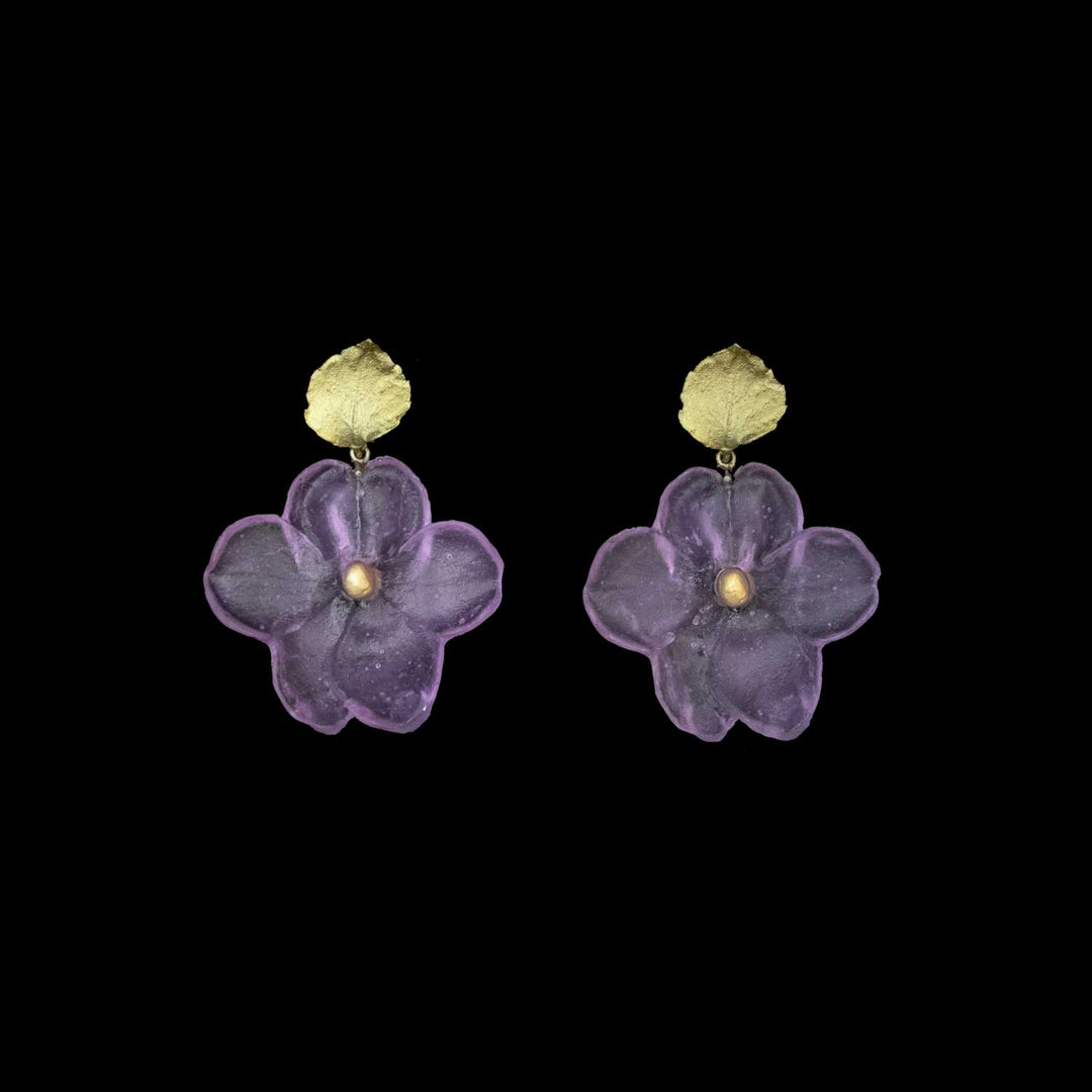 A pair of handcrafted floral earrings featuring green-colored circular studs with attached translucent purple flower-shaped pendants, displayed on a black background.
