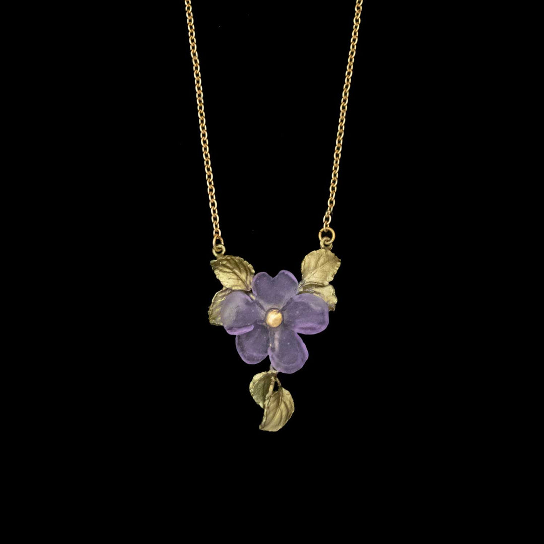 Gold necklace with a purple flower pendant, accented by gold leaves, forms a nature-inspired necklace reminiscent of Impatiens jewelry, beautifully displayed against a black background.