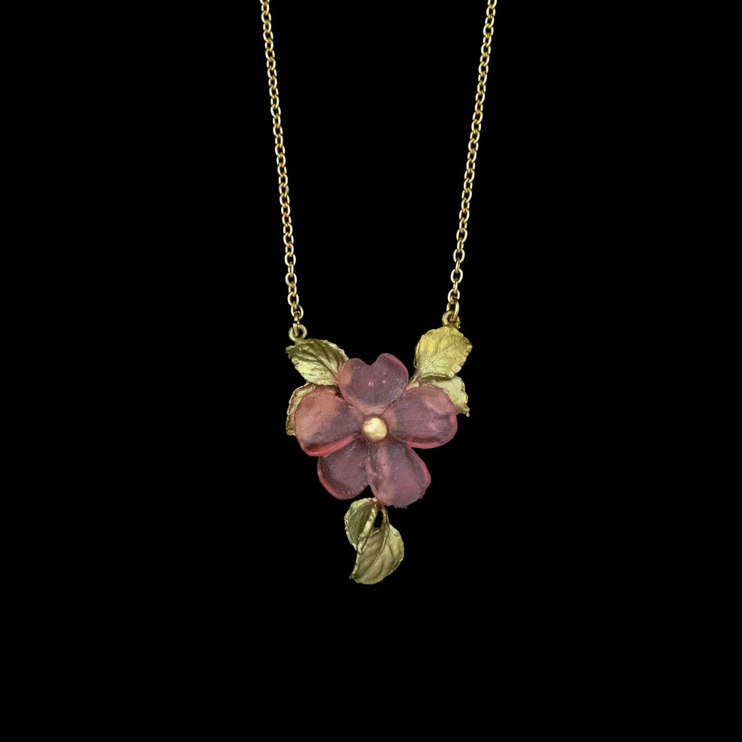 Gold chain necklace with a handcrafted flower pendant featuring a purple impatiens and green leaves against a black background—a beautiful, nature inspired necklace.