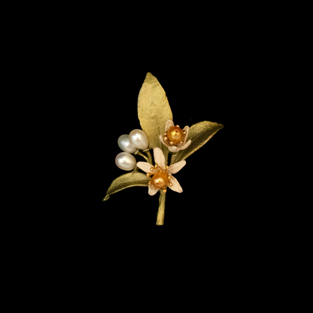 The Orange Blossom Lapel Pin – Web Exclusive features two white flowers with freshwater pearl centers, three small white pearls, and textured green leaves on a striking black background, inspired by botanical jewelry.