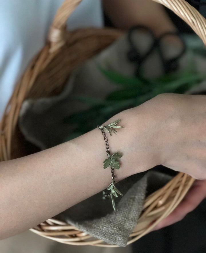 Hand wearing a bracelet with leaf charm in front of a woven basket