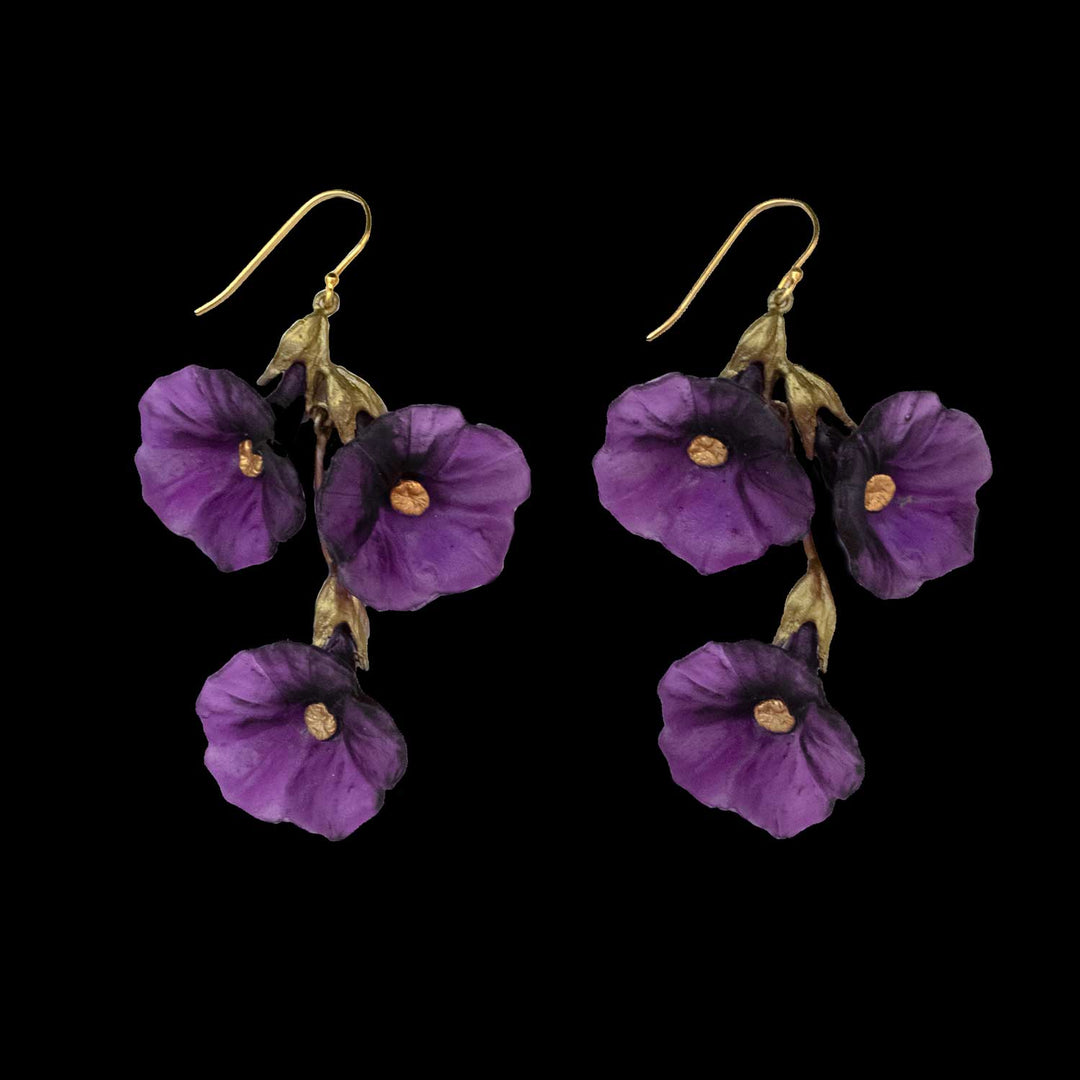 A pair of Petunia earrings featuring three purple flower-shaped elements on each, with gold hooks and a black background—an elegant piece of handcrafted jewelry inspired by nature.