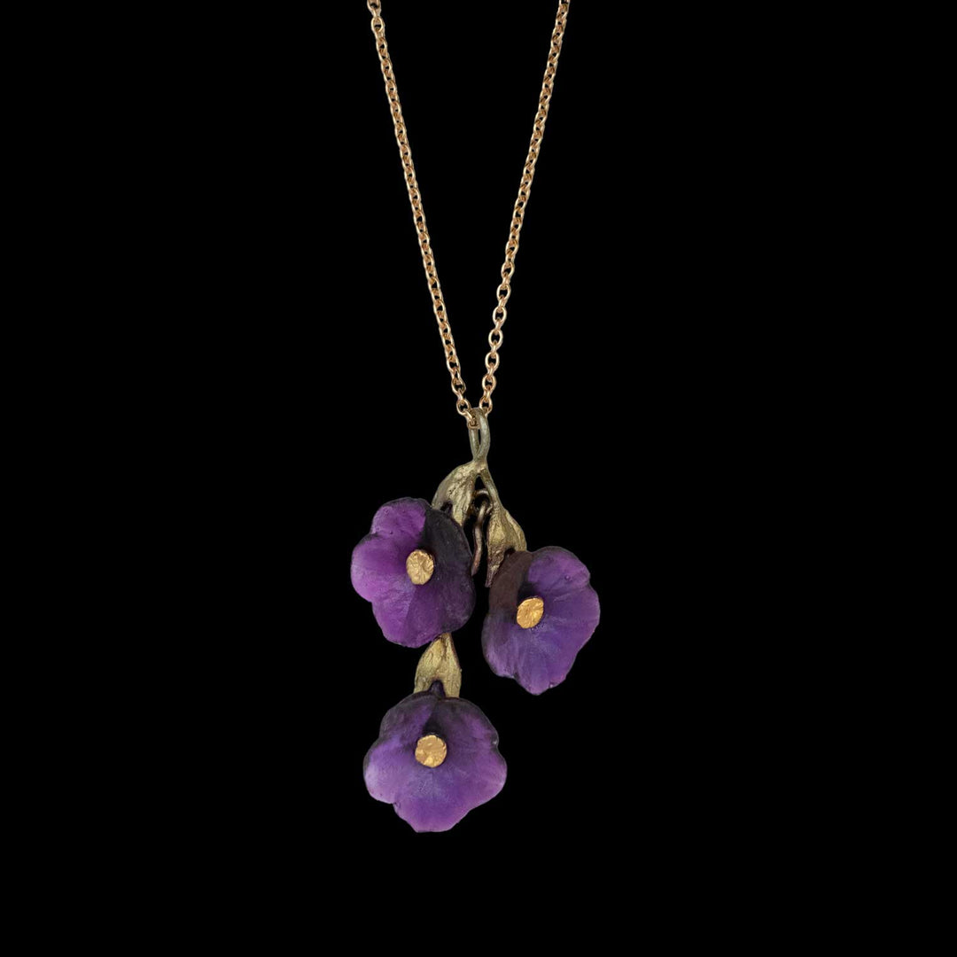 A gold necklace with a Petunia pendant featuring three purple flowers with yellow centers on a black background, showcasing nature-inspired artistry.