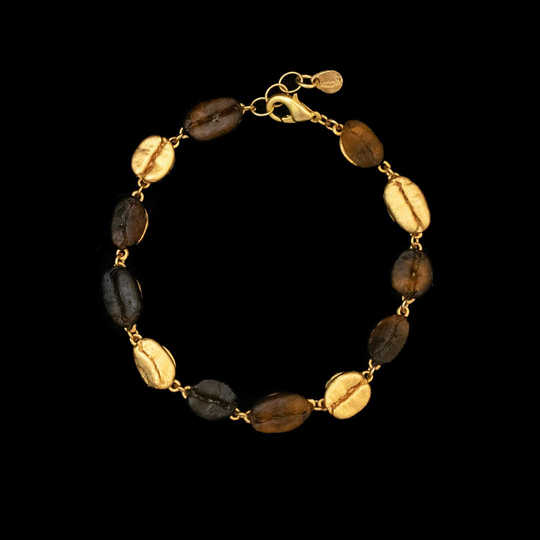 The Roasted Coffee Bean Bracelet showcases alternating gold-plated bronze and dark brown oval beans, linked by gold connectors and secured with a gold lobster clasp, set against a black background.