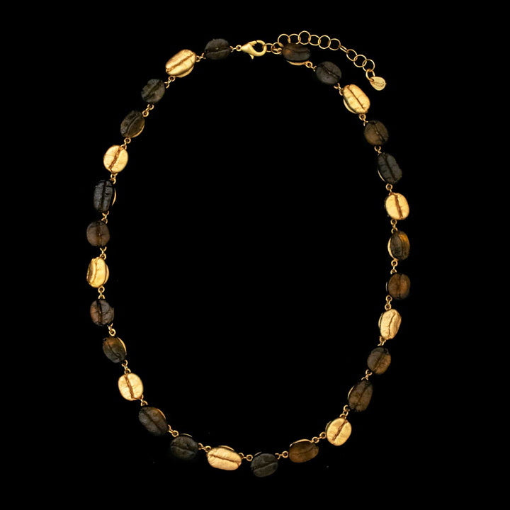 The Roasted Coffee Bean Necklace is gold-plated and features alternating gold and dark brown oval coffee beans, linked by small gold connectors, and showcased on a black background.