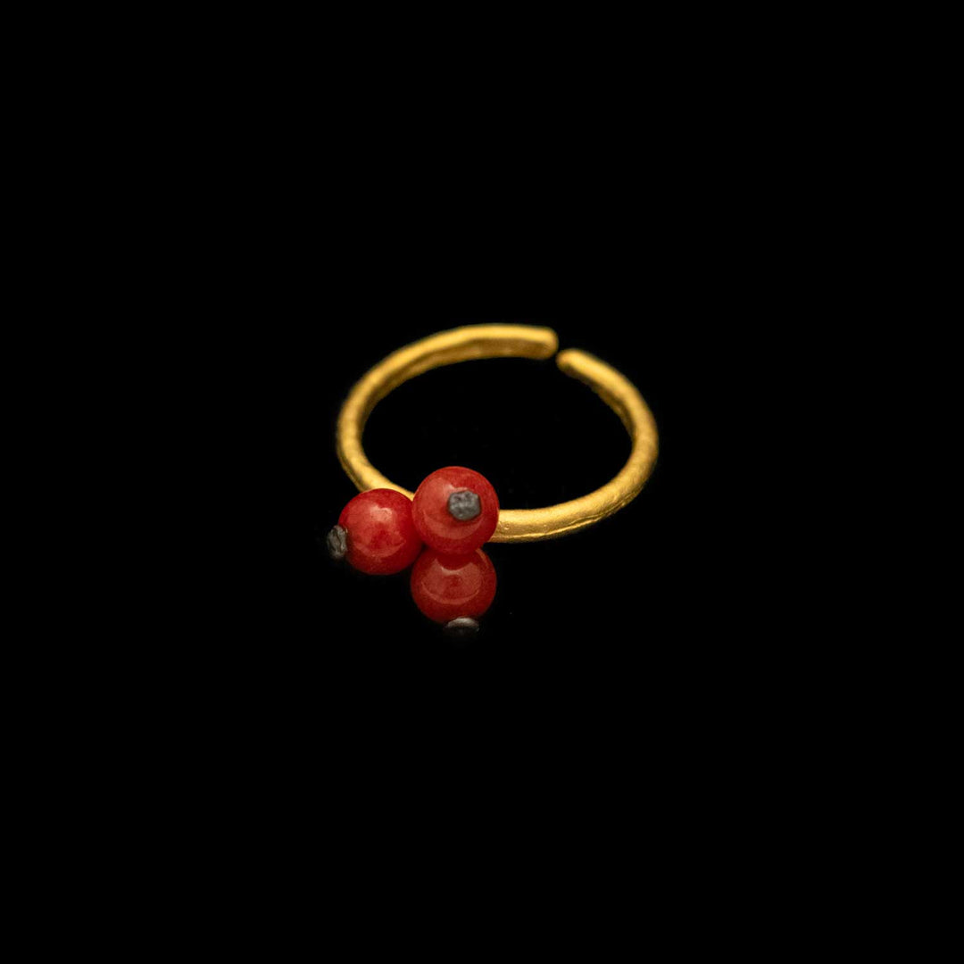 A gold-colored metal ring with a textured band and red jade accents, set against a black background.