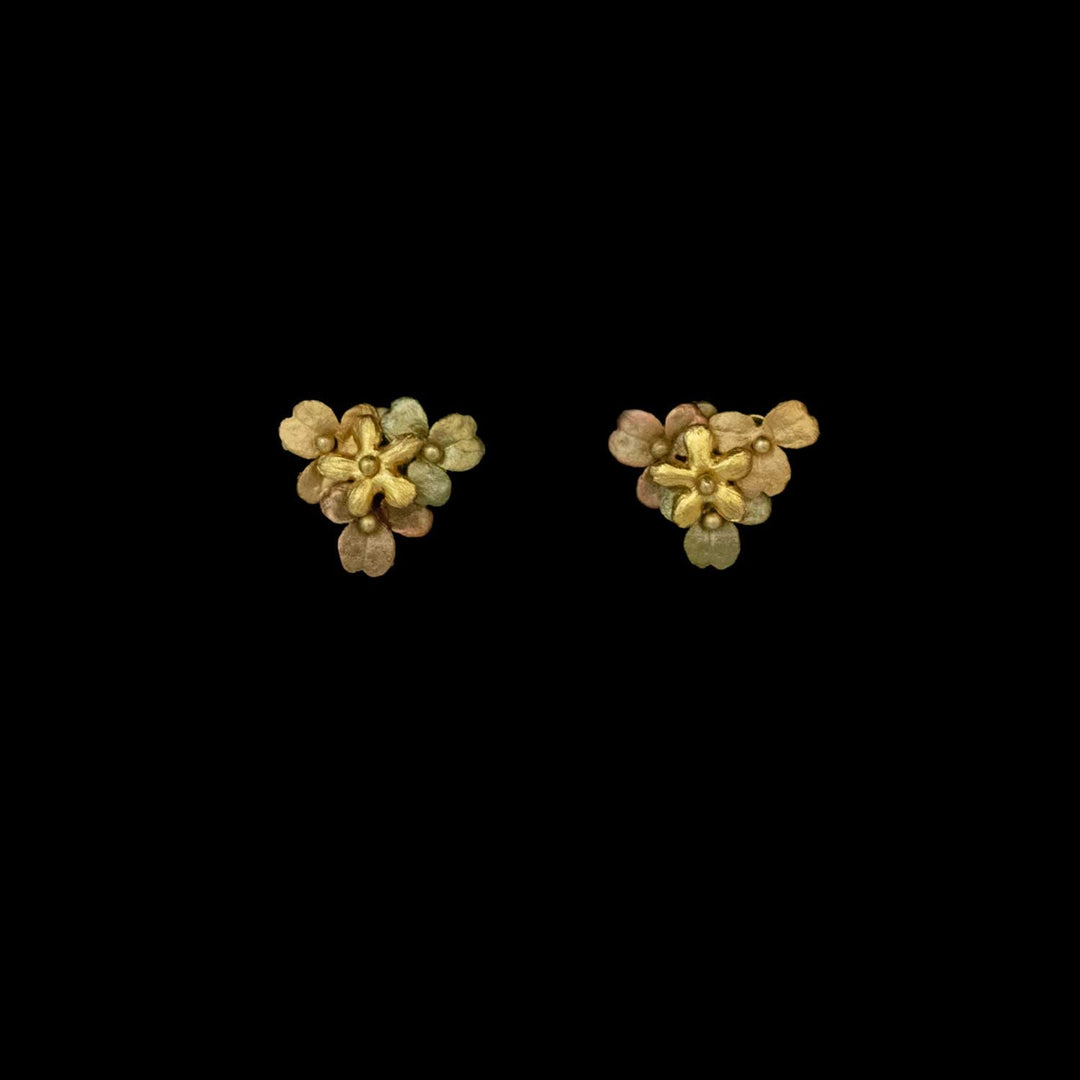 A pair of small, gold floral earrings with three-dimensional petals, inspired by wood sorrel jewelry, displayed on a plain black background.