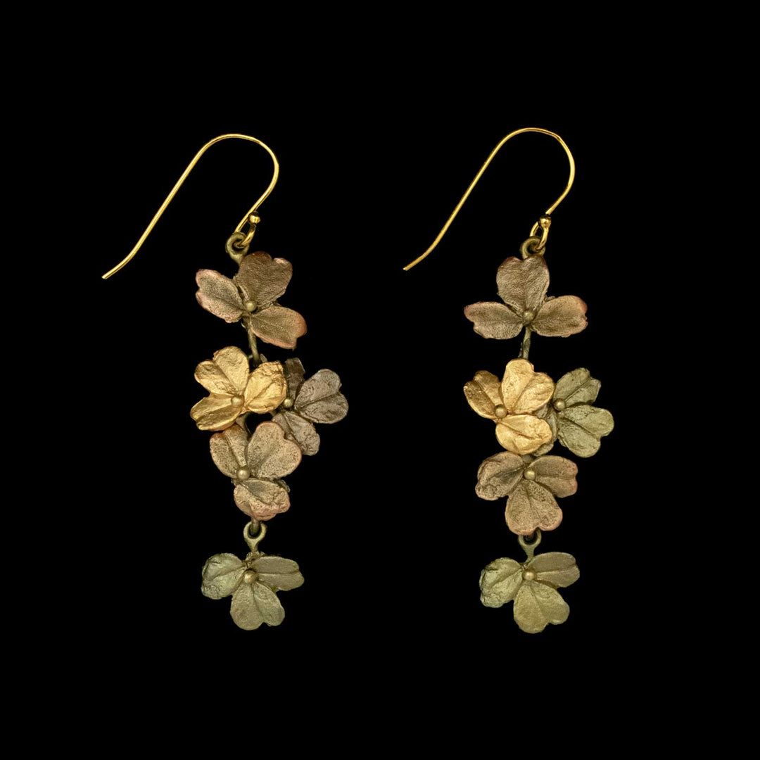 Gold-tone dangling earrings featuring three clusters of small, realistic flower shapes, inspired by wood sorrel jewelry, each with a hook for wearing, displayed on a black background. A perfect piece for lovers of nature inspired jewelry.
