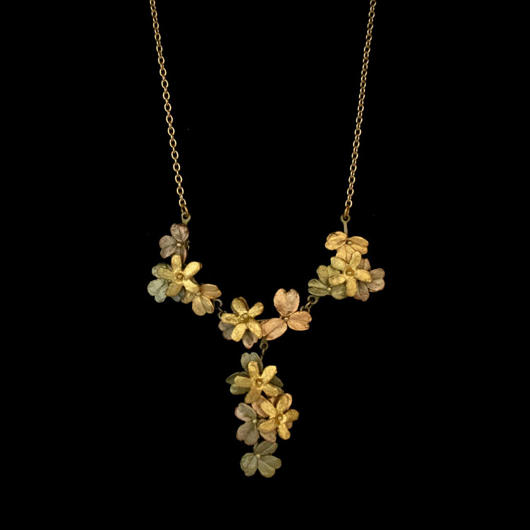 Gold necklace with a cluster of flower and leaf designs, featuring a Y-shaped arrangement, displayed on a black background—an elegant piece of nature inspired jewelry.