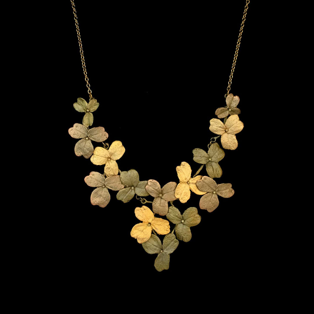 Gold, green, and bronze metallic necklace with overlapping leaves or petal shapes arranged in a clustered, V-shaped design on a thin chain, this nature-inspired jewelry evokes Wood Sorrel jewelry elegance against a black background.