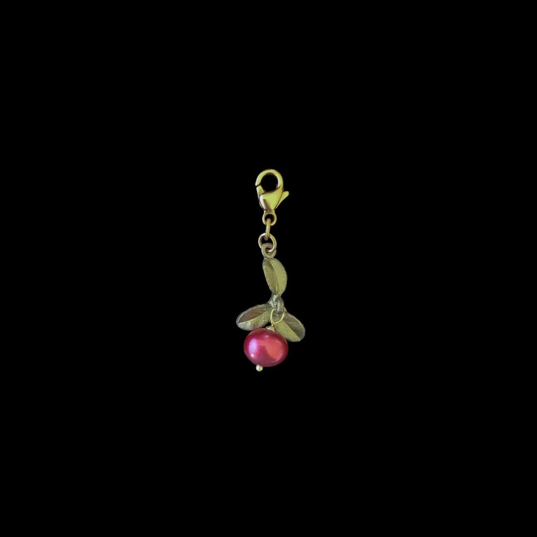 A red freshwater pearl charm with bronze leaves attached to a gold-colored clasp.