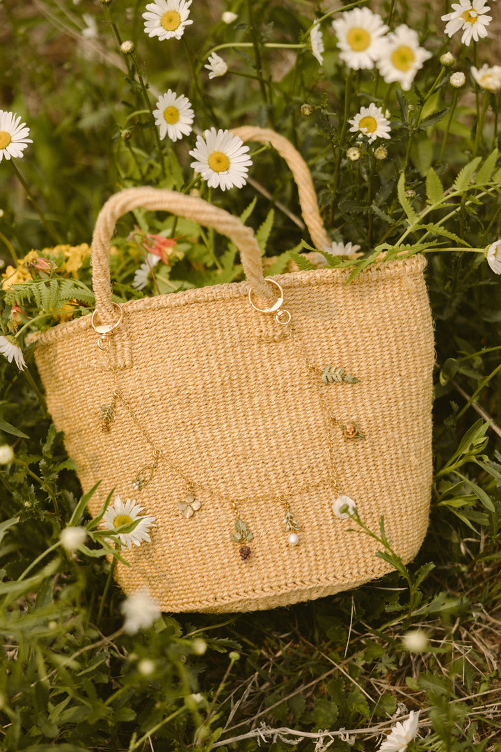 Woven handbag with decorative elements on a grassy background with daisies