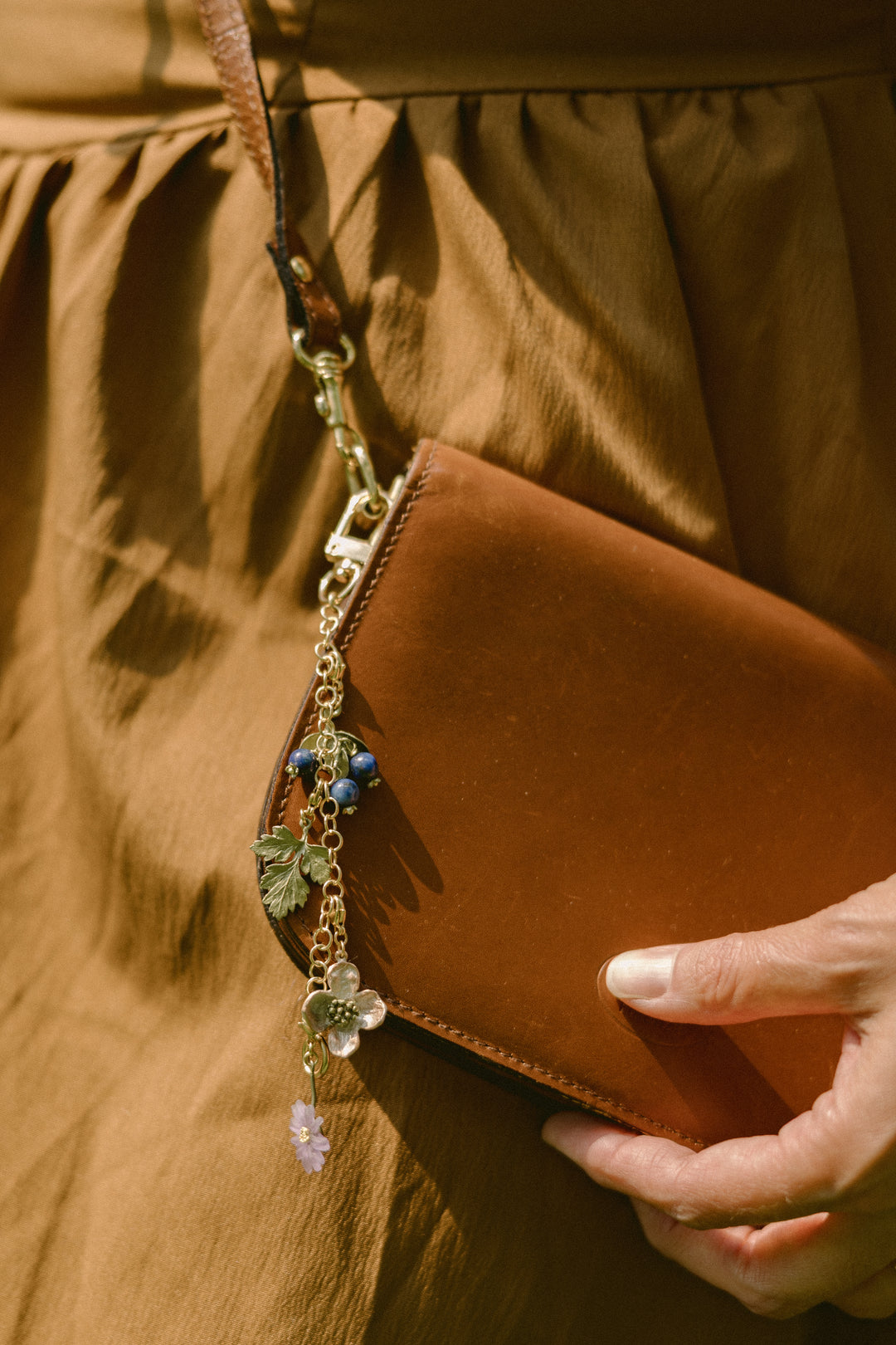 Brown leather clutch with decorative chain held by a person wearing a brown outfit.