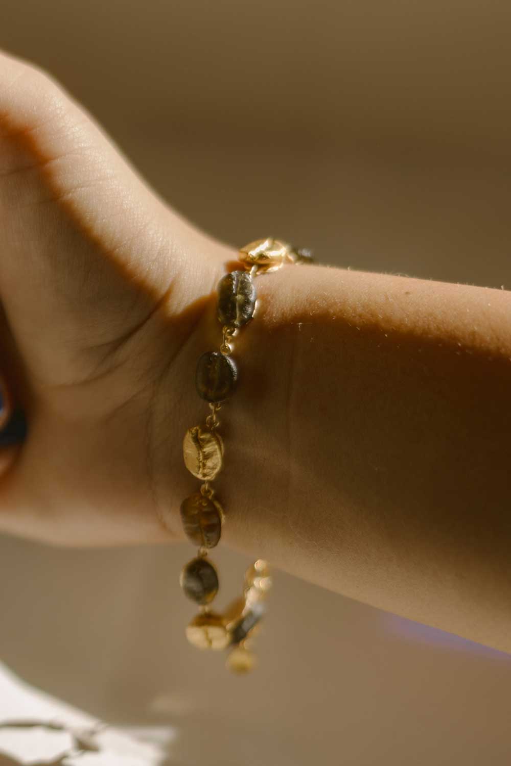 A close-up of a wrist wearing the Roasted Coffee Bean Bracelet, crafted in gold-plated bronze with coffee beans, captured in soft natural light.
