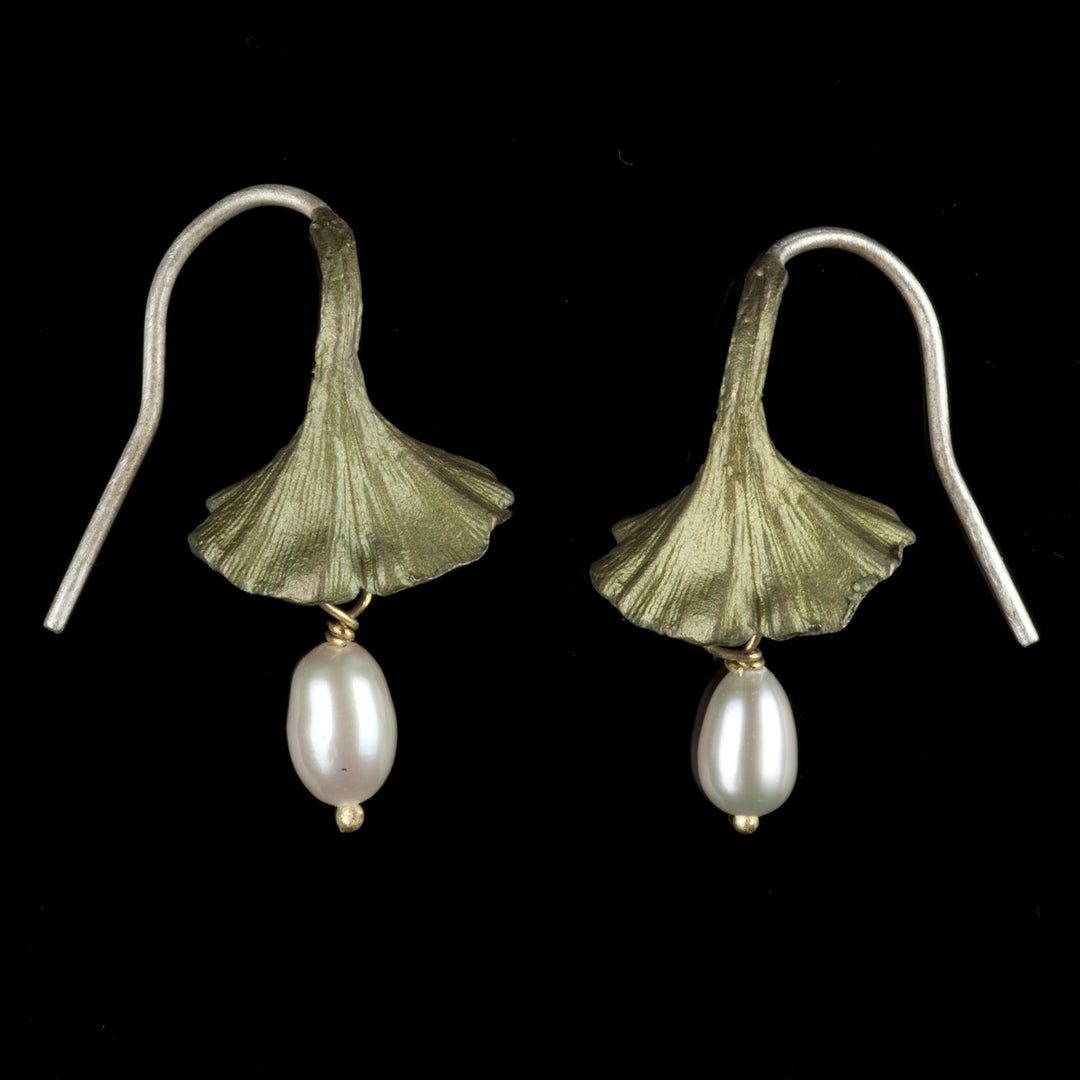 A pair of Ginkgo biloba leaf-shaped earrings with white freshwater pearls dangles, set against a black background.
