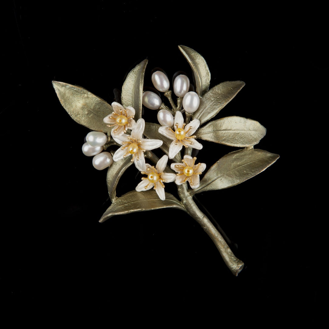 A brooch depicting white orange blossoms with green leaves and gold-tone accents, adorned with yellow and white pearls.
