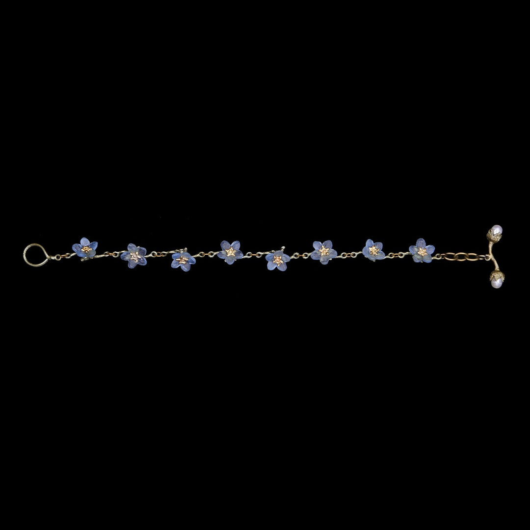 Delicate gold chain bracelet with small blue forget-me-not flower charms and pearl detail on toggle clasp.