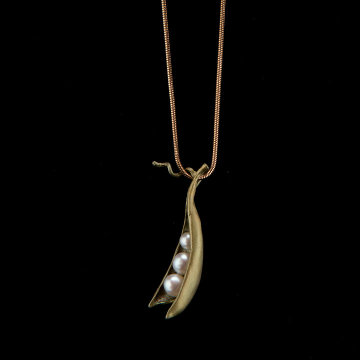 A bronze pea pod pendant with three white freshwater pearls, suspended from a brass chain against a black background.