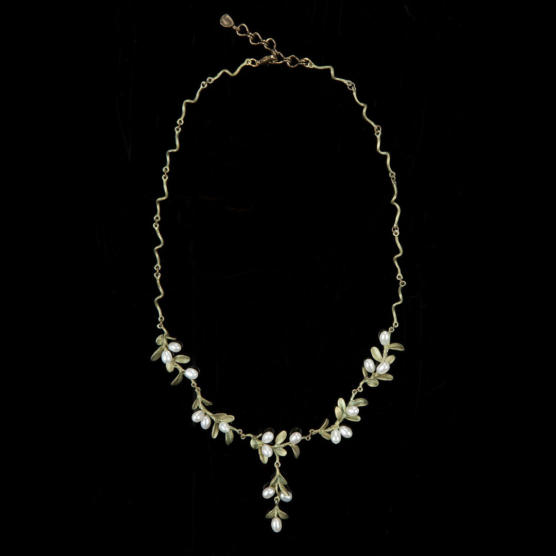 A green necklace with a wavy chain features small white pearls and leaf-like decorations in a floral pattern, with a central cluster forming a pendant. It is displayed against a black background.