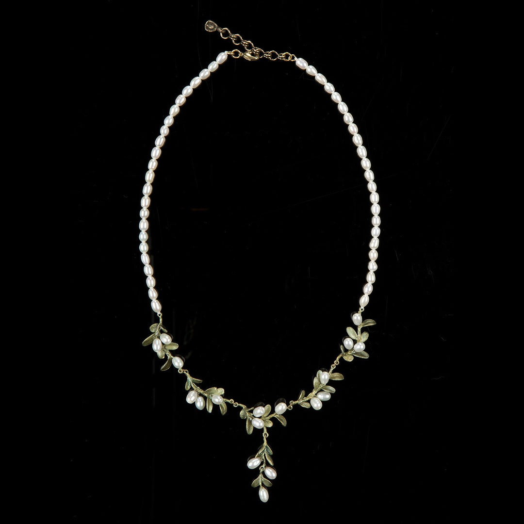 Delicate pearl necklace with gold chain and small green boxwood leaf accents.
