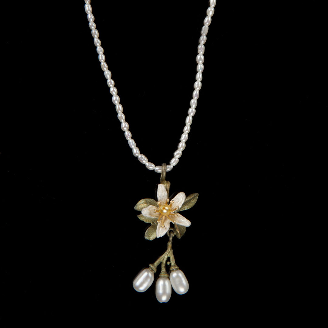 A necklace with a hand patinated bronze pendant featuring white and yellow freshwater pearls, designed to resemble an orange blossom flower.