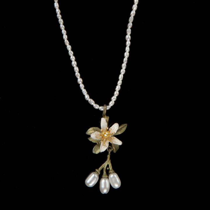 A necklace with a hand patinated bronze pendant featuring white and yellow freshwater pearls, designed to resemble an orange blossom flower.