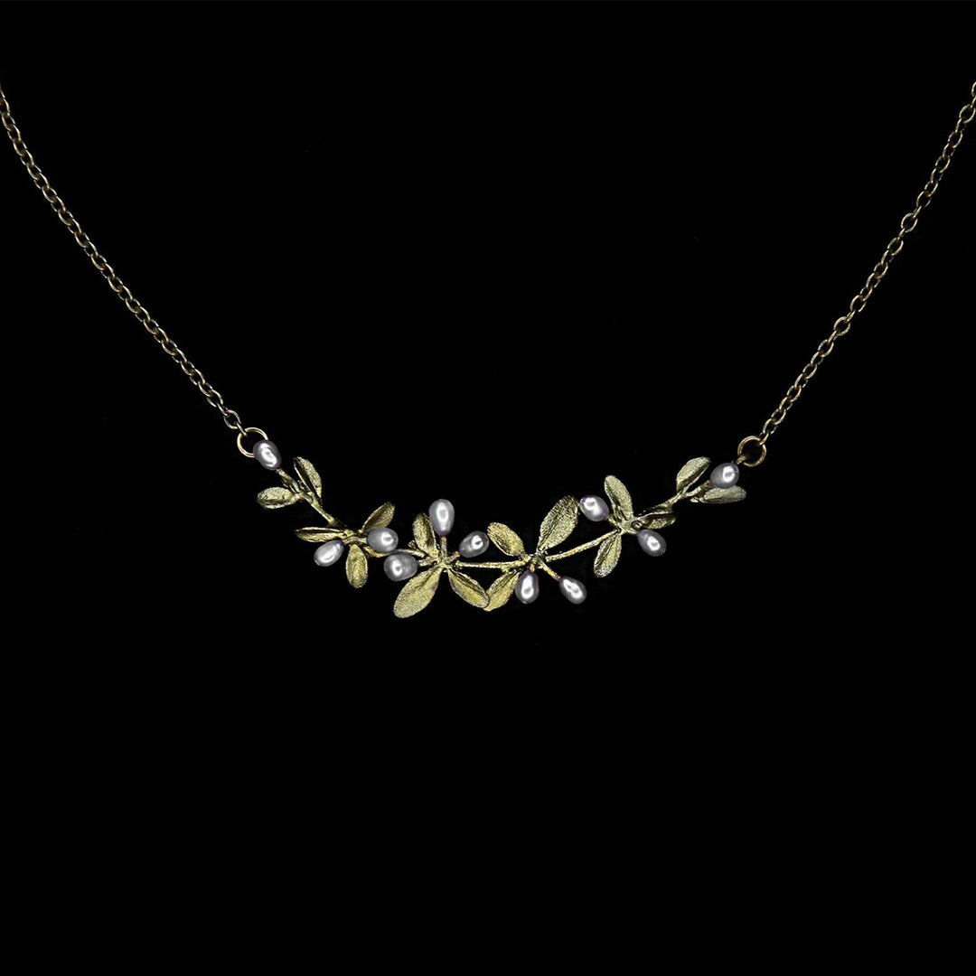 A bronze necklace with a cluster of small leaves and white pearl accents, set against a black background.