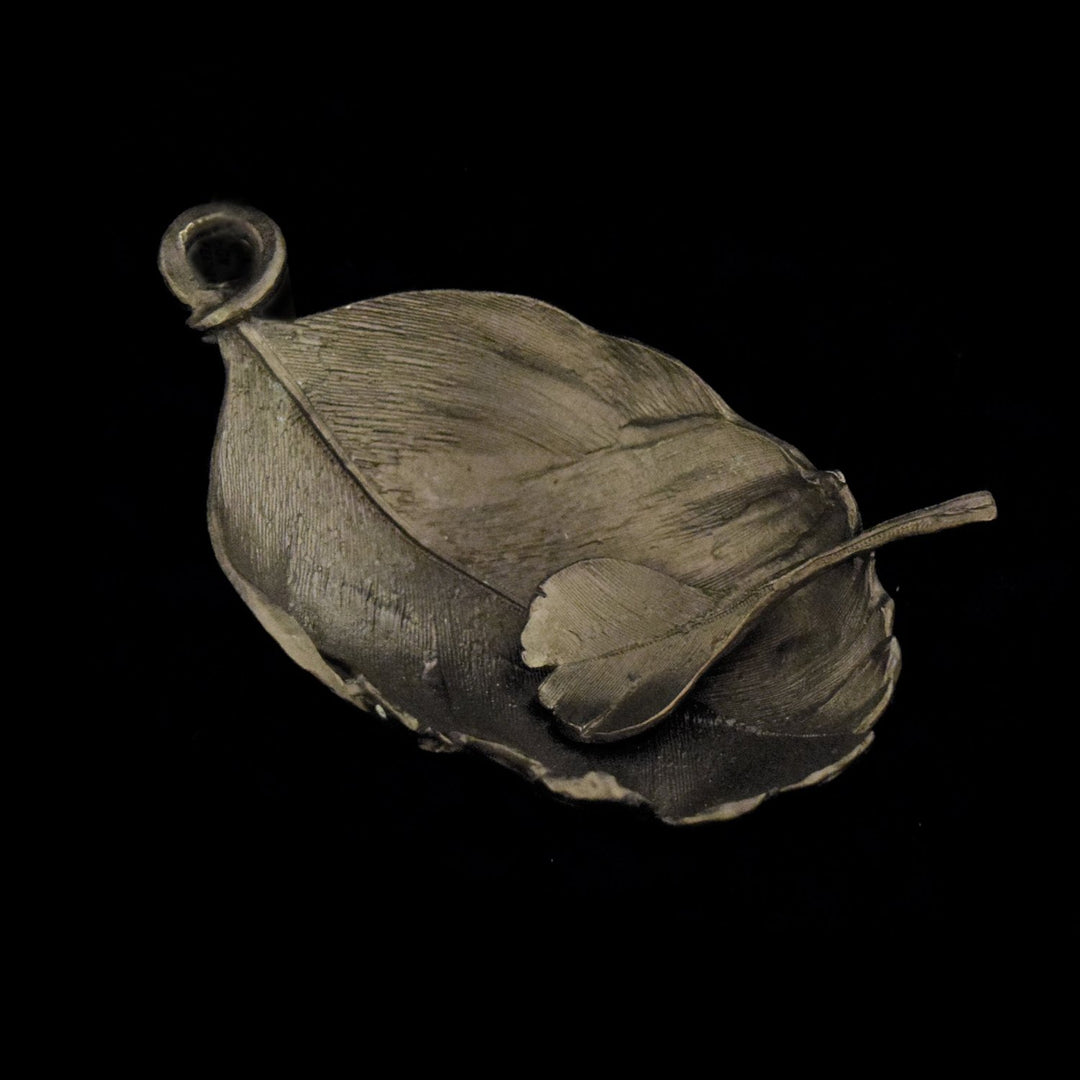 A gunmetal feather-shaped salt dish made of pewter, with a textured design resembling natural foliage.