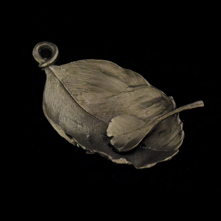 A gunmetal feather-shaped salt dish made of pewter, with a textured design resembling natural foliage.