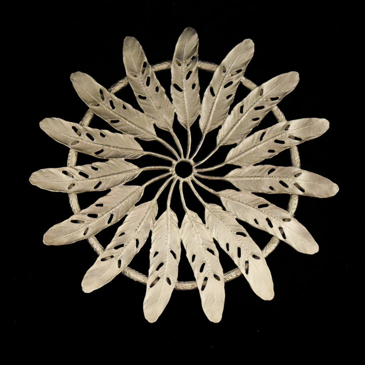 A silver pewter trivet with a feather design.