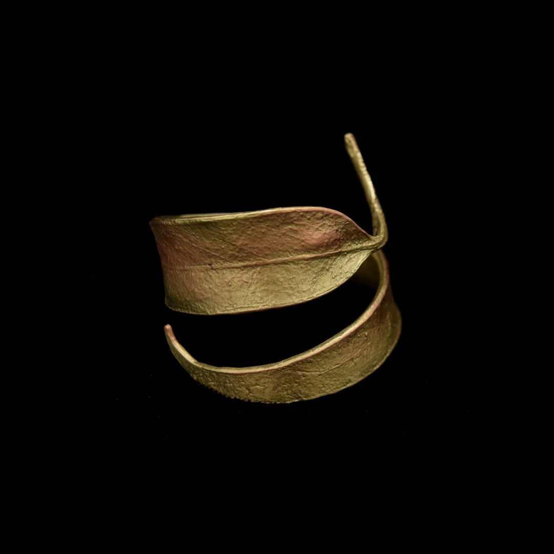 A gold-colored, textured metal napkin ring shaped like overlapping leaves is displayed against a solid black background.