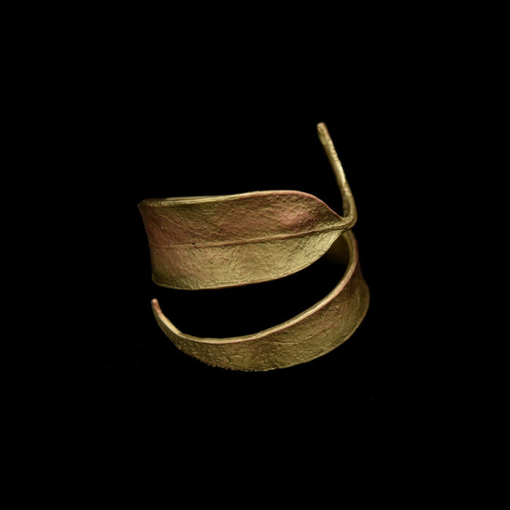 A gold-colored, textured metal napkin ring shaped like overlapping leaves is displayed against a solid black background.