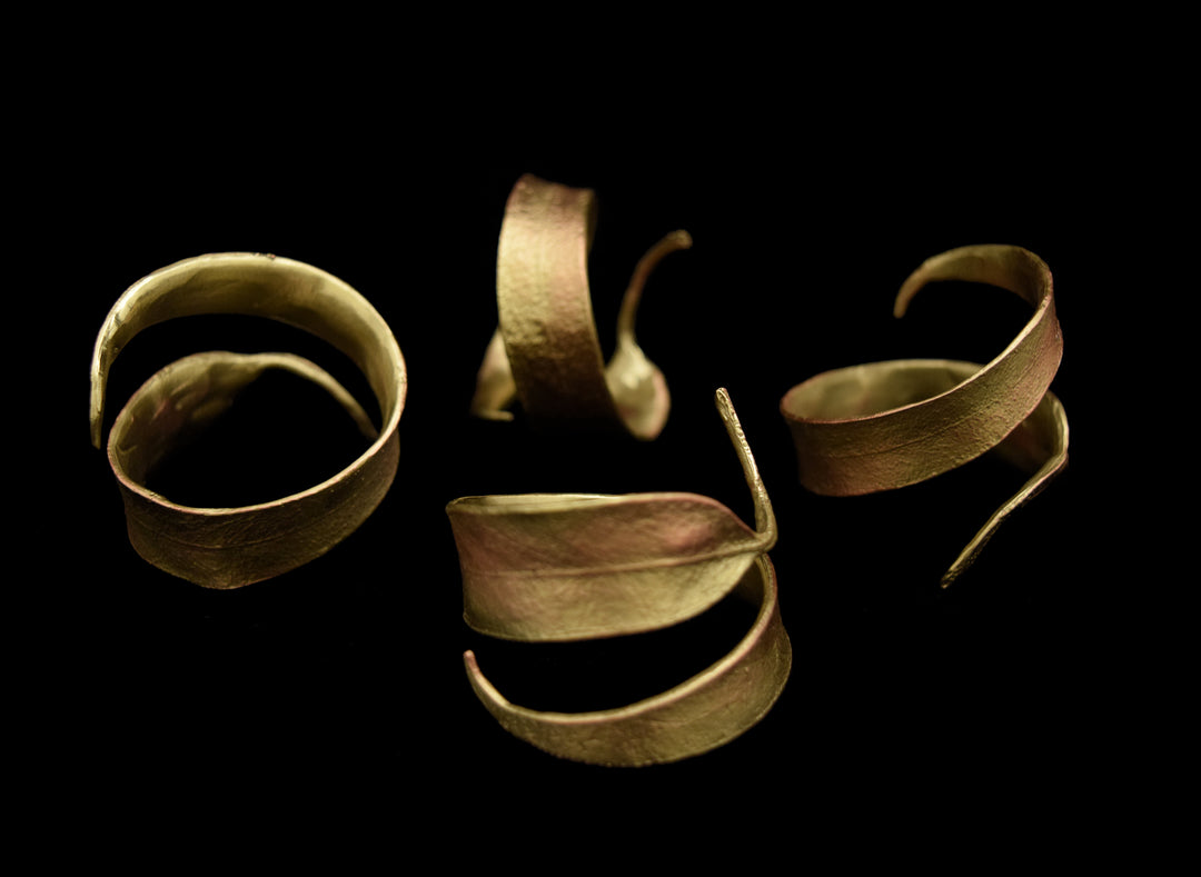 Four textured, gold-colored napkin rings with open spiral designs are arranged on a black background. 