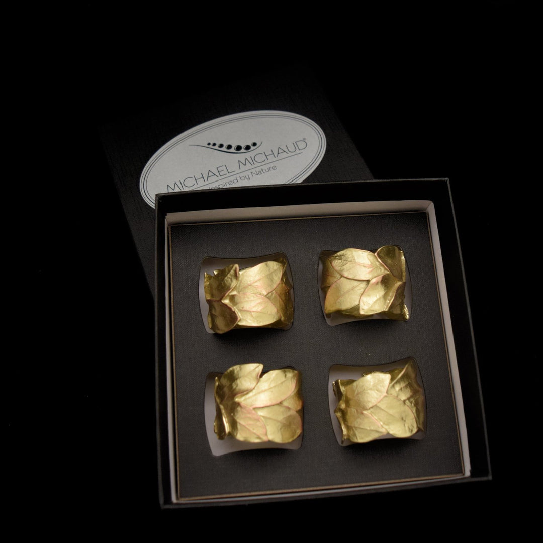 4 napkin rings in gold with a leaf design sit in a black presentation box