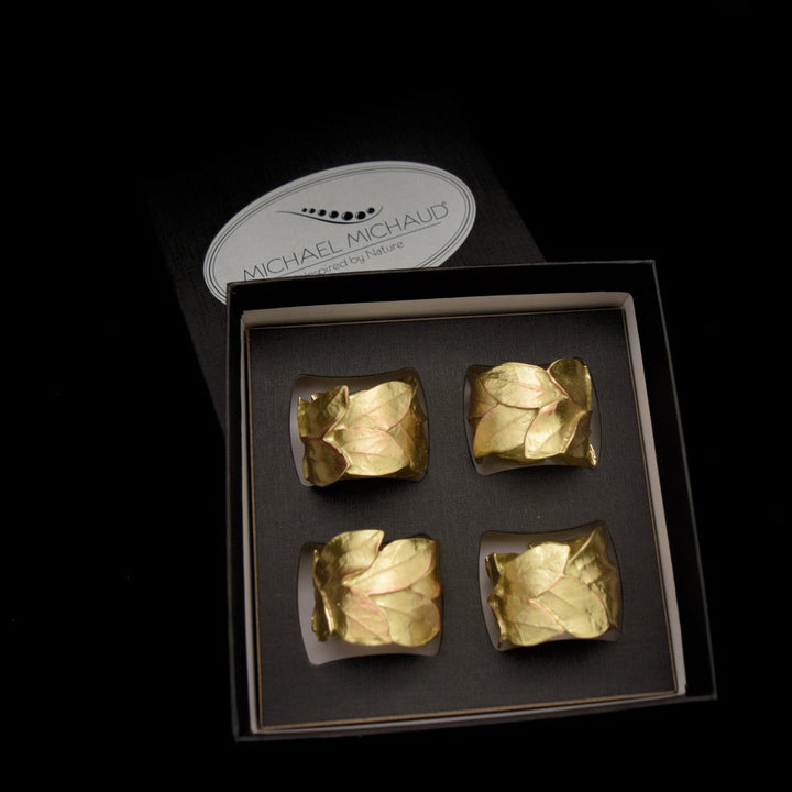 4 napkin rings in gold with a leaf design sit in a black presentation box