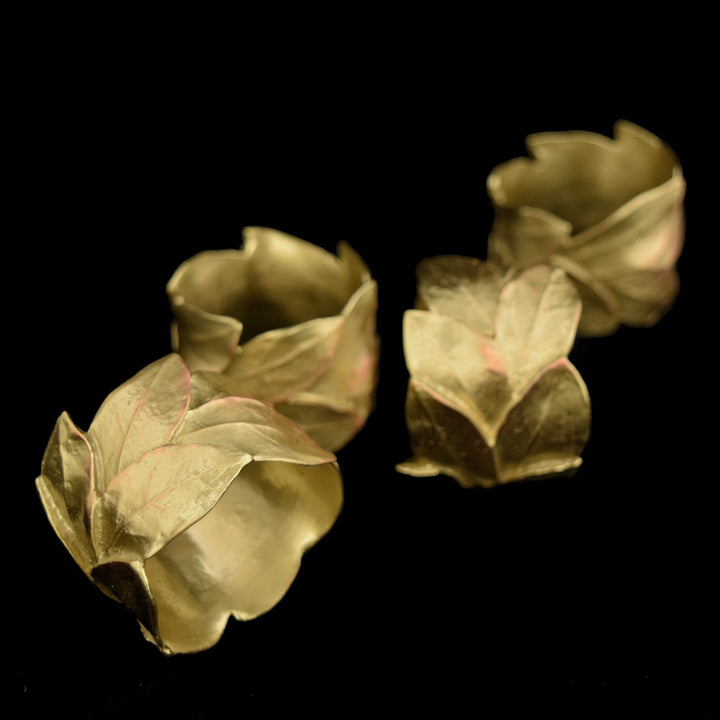 A set of three bronze-finished pewter napkin rings with a leaf design, displayed against a dark background.