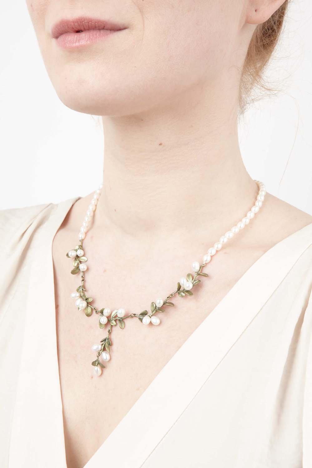 Delicate pearl necklace with small green boxwood leaf accents and gold-tone details, worn with cream blouse.