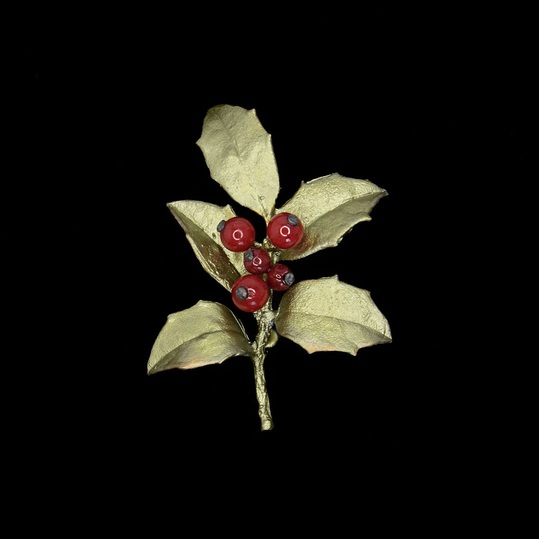 A decorative brooch shaped like a holly branch, featuring gold-colored leaves and red berry-like beads, set against a black background.