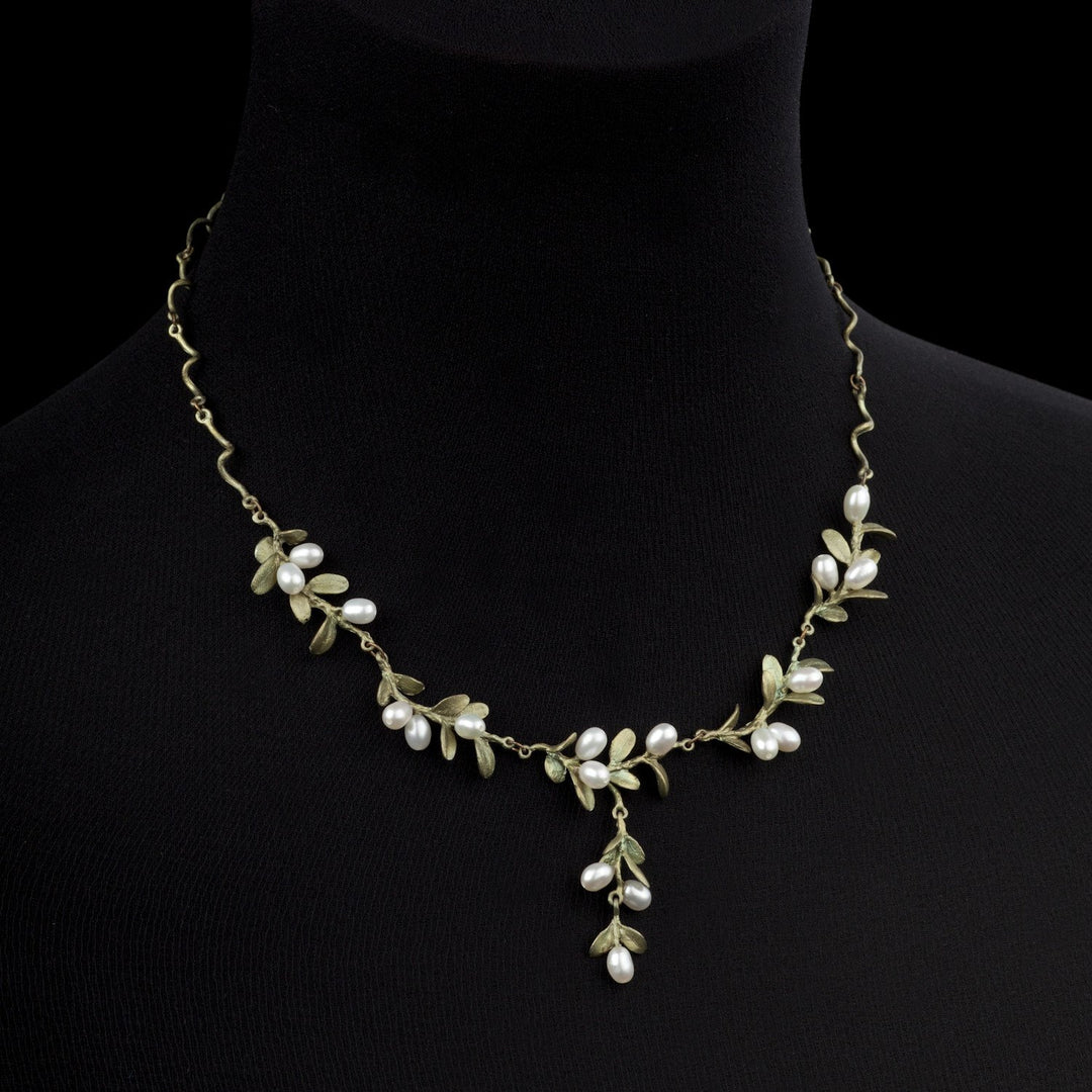 A boxwood necklace inspired by Mount Vernon jewelry, featuring gold-toned metal branches and leaves with clusters of small white pearls, all beautifully displayed on a black velvet bust.