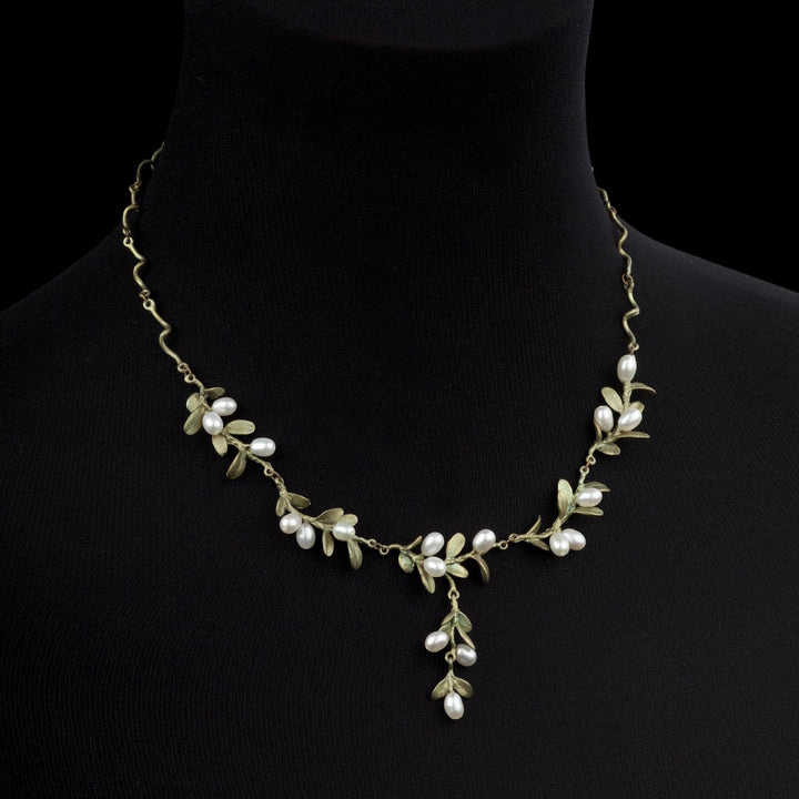A boxwood necklace inspired by Mount Vernon jewelry, featuring gold-toned metal branches and leaves with clusters of small white pearls, all beautifully displayed on a black velvet bust.