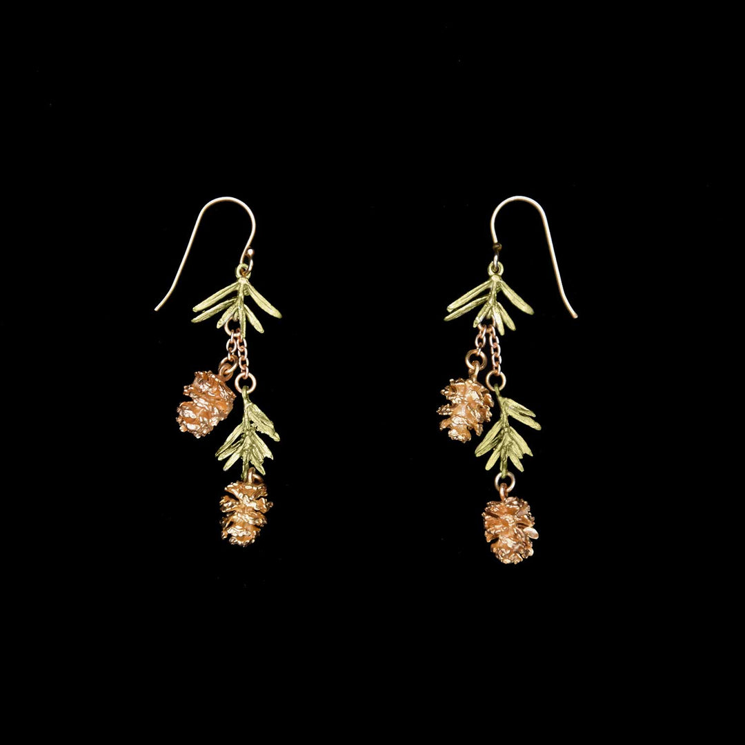 A pair of dangling earrings featuring gold pine cones and green pine needle-like leaves, hanging from gold hooks, displayed against a black background.