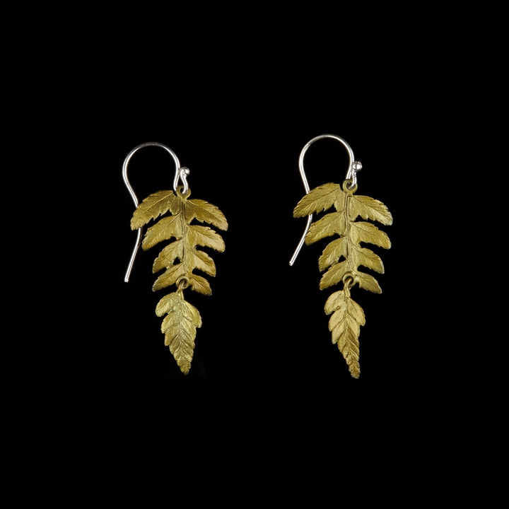 A pair of fern leaf earrings with green patinated leaves on a black background, crafted in bronze with gold plated silver hooks.